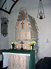 St Melangell's shrine. A pinkish carved stone structure with an altar attached to the front, decorated with a crucifix, candles, and flowers.