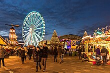 A brightly lit fair with German-style market stalls and a ferris wheel