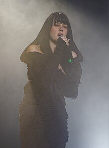 Teya Dora wearing a black outfit, singing onstage, surrounded by smoke