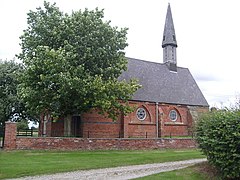 A small brick buot church with a sharp steeple on the right hand side
