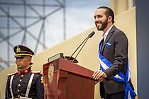 Nayib Bukele standing at a podium and speaking to a large crowd.