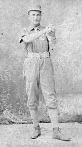 A baseball player is standing in his uniform, holding a baseball.