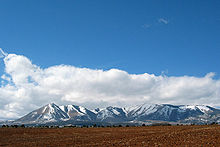 Snow-covered mountains protruding from a plain with tilled soil in the foreground.