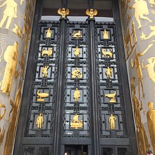 A large metal door is flanked with golden creatures and persons.