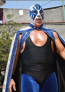 A masked wrestler wearing a cape during an outdoor wrestling event.
