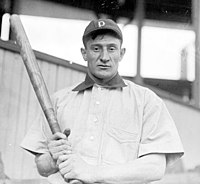 A man wearing a white baseball jersey and dark baseball cap with an ornate "P" on the face and with a grimace on his face