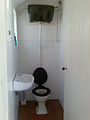 A toilet room with an older style flush toilet. The chain (on the upper right) is pulled to empty the elevated cistern (tank).