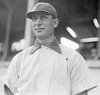 A man wearing a white baseball jersey and dark baseball cap