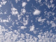 Small shreds of white altocumulus clouds against a blue sky.