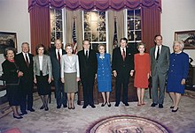Husbands and wives alternate, as the subjects of the photo line up for the shoot, with the Presidential Seal in the foreground.