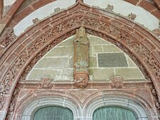 The entrance door to the church via the south porch. Over the door is a depiction of Saint Herbot with the inscription "MESSIRE IEHAN DE LAVLNAY P[RE]B[T]RE GOUVERNEUR DE CEANS FIST FAIRE CEST PORTAL COMENCE(ME)NT LE PREMIER IOVR DE IVIET LAN MIL QVATRE CE[N]TS QVATRE VINTS DIX OVIT"