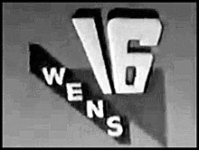 A black-and-white slide. On a gray background, a white 16 towers over a triangular-shaped area in dark gray. The letters WENS run in an incomplete stripe to the left diagonally from middle-left to the bottom.