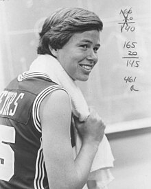 A young woman with short and fair hair and wearing a basketball jersey smiling.