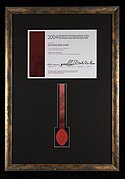 Photograph of The Coventry International Prize for Peace and Reconciliation certificate and seal awarded to Dr Madeleine Sharp in 2004. The award is a framed certificate with a red ribbon and wax seal below.