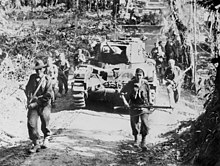 Infantrymen advance along a jungle track in concert with a supporting tank