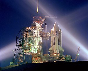 A timed exposure of the first Space Shuttle mission, STS-1, at Launch Pad A, Complex 39, turns the space vehicle and support facilities into a night-time fantasy of light. To the left of the Shuttle are the fixed and the rotating service structures.