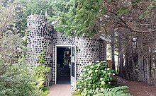 Small building entirely made out of glass bottles with a door open