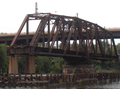 The Philadelphia, Wilmington and Baltimore Railroad Bridge, built 1901-1902 by the American Bridge Company across the Schuylkill River in the Grays Ferry neighborhood in Philadelphia, Pennsylvania, abandoned in open postion ca. 1976. Swing span, 226'-7" long, stone center pier with wood fenders and pilings, and western girder approach. Modern Grays Ferry Avenue bridge in background.