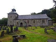 View of the church from the churchyard: a stone church with a square tower and a small porch, surrounded by old gravestones.
