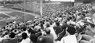 A black and white photograph of a baseball game in progress with fans looking on and few empty seats in sight