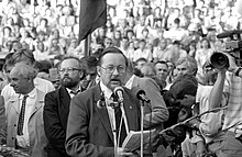 A middle-aged man speaking in front of a crowd