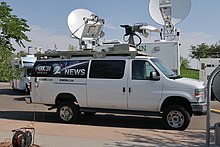 A white van with KDVR and KWGN-TV logos and microwave and satellite dishes on its roof