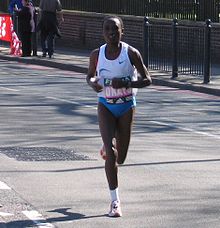 Black woman running in white top and blue bottoms on a road.