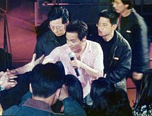 Cheung in a white shirt performing, surrounded by bodyguards