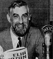 A smiling Alan Douglas holding a book by Elia Kazan, directly next to him is a microphone with ribbons reading "WKYC" at the top and "NBC" on the sides.