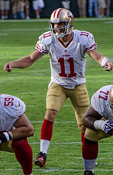 Alex Smith in a San Francisco 49ers uniform behind two linemen, about to take a snap.