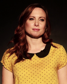 A 35-year-old woman with red hair and a yellow shirt looking to the right of the camera.