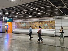 People walking past a brass mural displayed at the concourse level