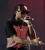 A man wearing sunglasses raps into a microphone.