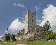 Photograph of a medieval stone-built tower with ruined walls against the sky