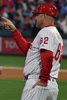 A man in a white baseball jersey with red undersleeves and cap