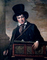Very young white man, clean-shaven, wearing a top hat and carrying a portable barrel organ