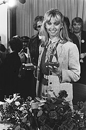 A woman with long blonde hair holding two trophies