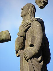 The statue of John the Evangelist on the cross' crosspiece. He has a book tucked under his left arm