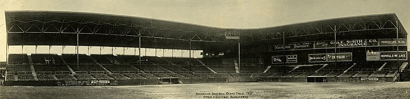 a black and white photograph of the bleachers at a ballpark with an overhanging roof above taken from the playing field