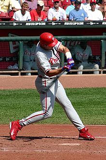 A man in a Philadelphia Phillies' uniform swinging a baseball bat