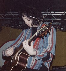 A man performing live on-stage with an acoustic guitar.