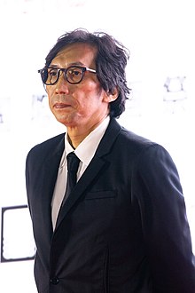Yukisada at press event in three-quarter profile wearing suit