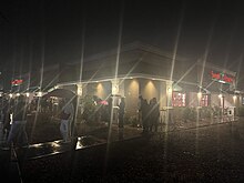 A Sweet Tomatoes Location in the Night with a long line wrapped around the building