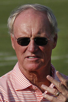 Unposed head and shoulders photograph of Schottenheimer wearing a red-and-white striped polo shirt and dark sunglasses