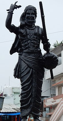 A black statue of an aged man holding a tambura in his hand