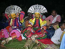 Two seated, costumed people with others
