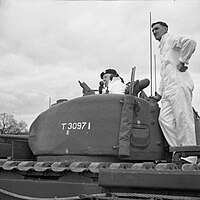 A photo showing Winston Churchill speaking into a radio while poking out of a turret of a Churchill tank.