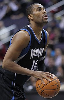 A basketball player wearing a black jersey with blue and white trim while taking a free throw.