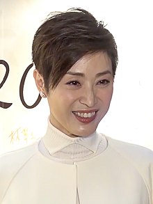 Chan, with short hair and dressed in a white top, looking right being photographed against a white background.