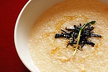 Light golden colored porridge is topped with strips of green and drizzles of oil